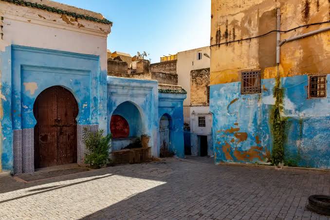 A courtyard in the Mellah of Fes showing the distinctive blue-painted walls, cobblestone paving and arched doorways that characterise the historic Jewish quarter — now largely inhabited by Muslim Moroccan families but retaining its architectural identity unchanged